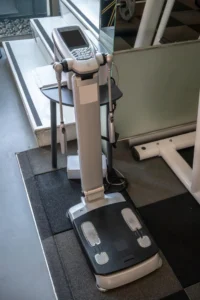 clinical-bia-body-composition-analyzer-machine-2026 Clinical bioelectrical impedance analyzer machine with hand electrodes and foot pads used for body composition measurement in a fitness or medical setting.