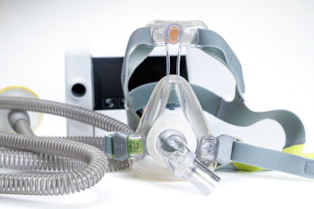 cpap-full-face-mask-and-tubing Full-face CPAP mask with headgear and tubing connected to a CPAP device, shown close up.